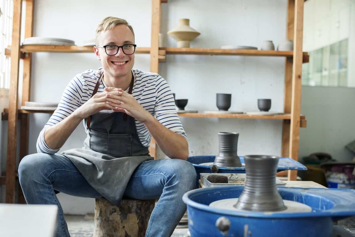 Creative man smiling in pottery studio, exploring mental health and creativity link.