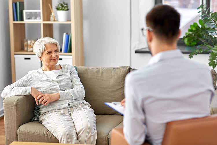 Elderly woman in therapy session discussing life changes with counselor.
