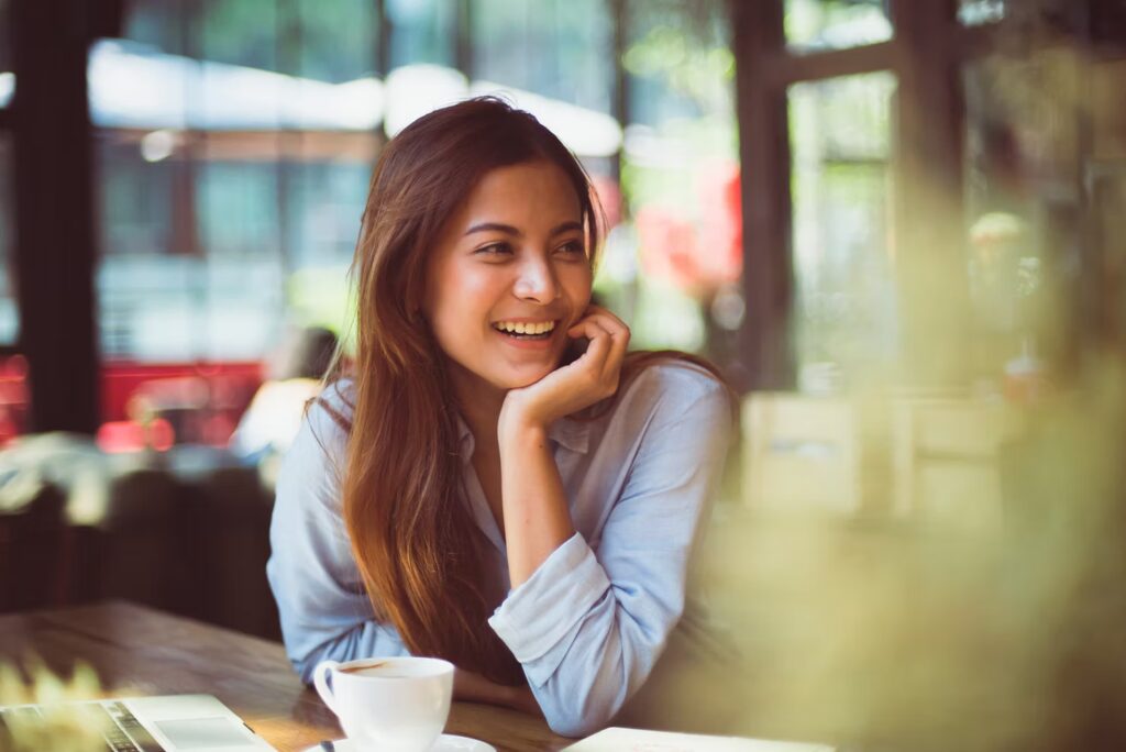 Woman smiling and sitting at a café table with a cup of coffee, looking to the side